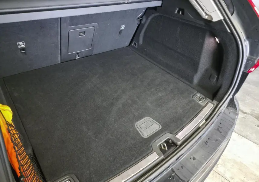 Vue intérieure du coffre ouvert du Volvo XC60 noir, montrant le tapis noir et les fixations latérales.