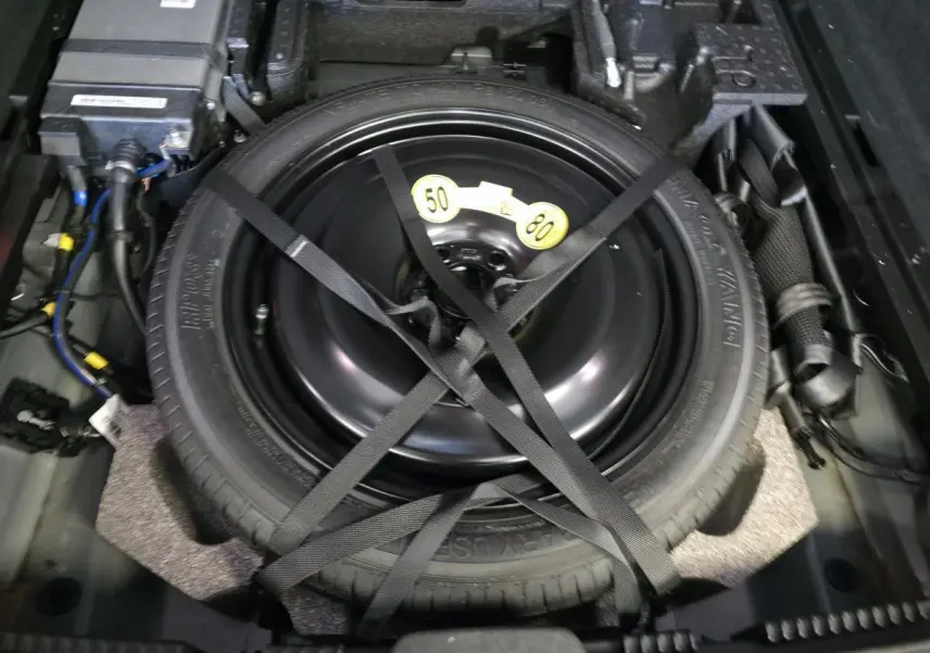 Gros plan sur la roue de secours temporaire noire fixée dans le coffre du Volvo XC60 Ultimate Style Dark 2023.
