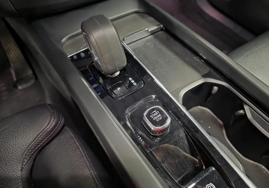 Gros plan sur la console centrale noire du Volvo XC60 2023, avec levier de vitesse et bouton Start/Stop.
