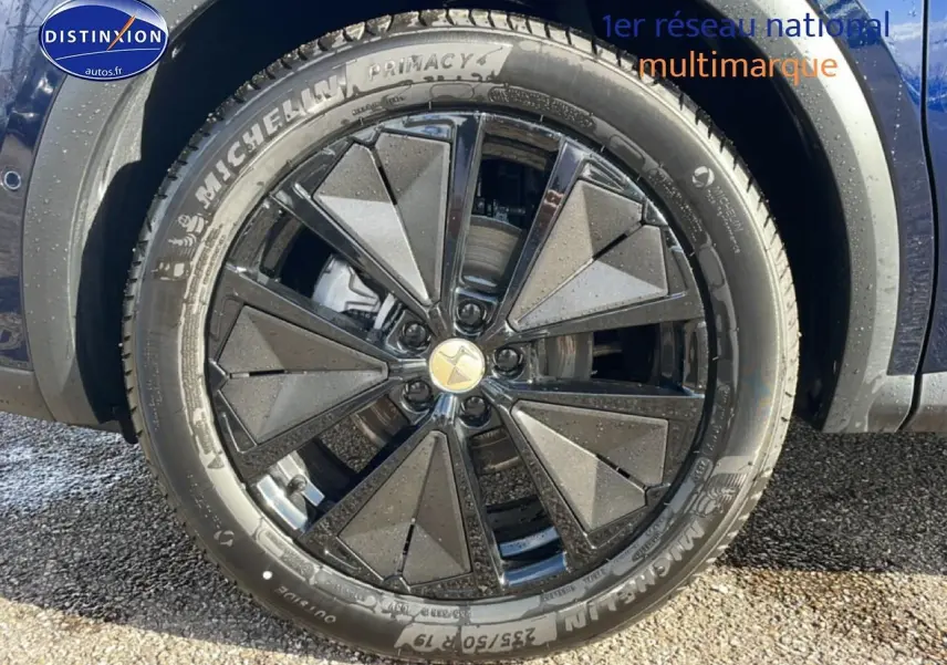 Gros plan sur la jante noire au design géométrique du DS7 bleu, mettant en valeur le pneu Michelin.