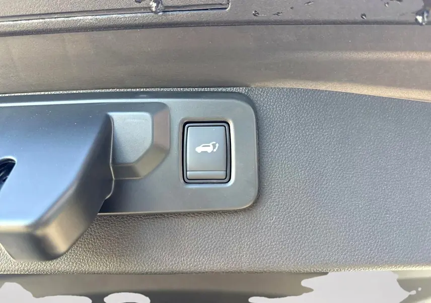 Gros plan sur le bouton d'ouverture électrique du coffre dans le coffre d'une Renault Symbioz gris rafale.