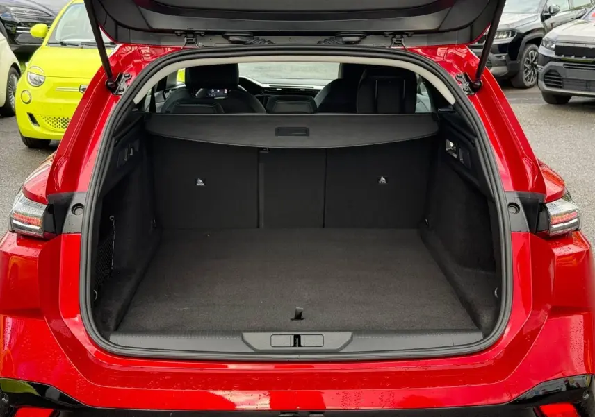 Coffre ouvert vu de l'arrière d'une Peugeot 308 SW rouge Elixir avec banquette arrière et cache-bagages visibles.
