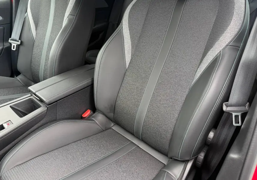 Gros plan sur les sièges avant en tissu et cuir gris avec surpiqûres bleues dans l’habitacle d’une Peugeot 308 SW rouge.