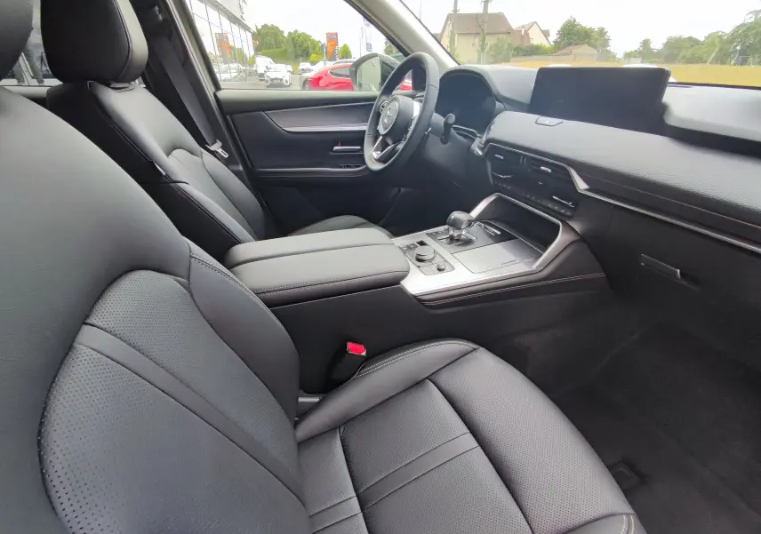 Vue intérieure côté conducteur du Mazda CX-60 2024, sièges cuir noir et tableau de bord moderne avec écran central.