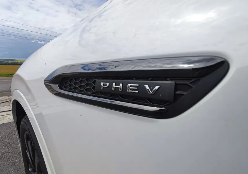 Gros plan sur l'aile avant gauche blanche métallisée du Mazda CX-60 avec l'emblème PHEV noir brillant.