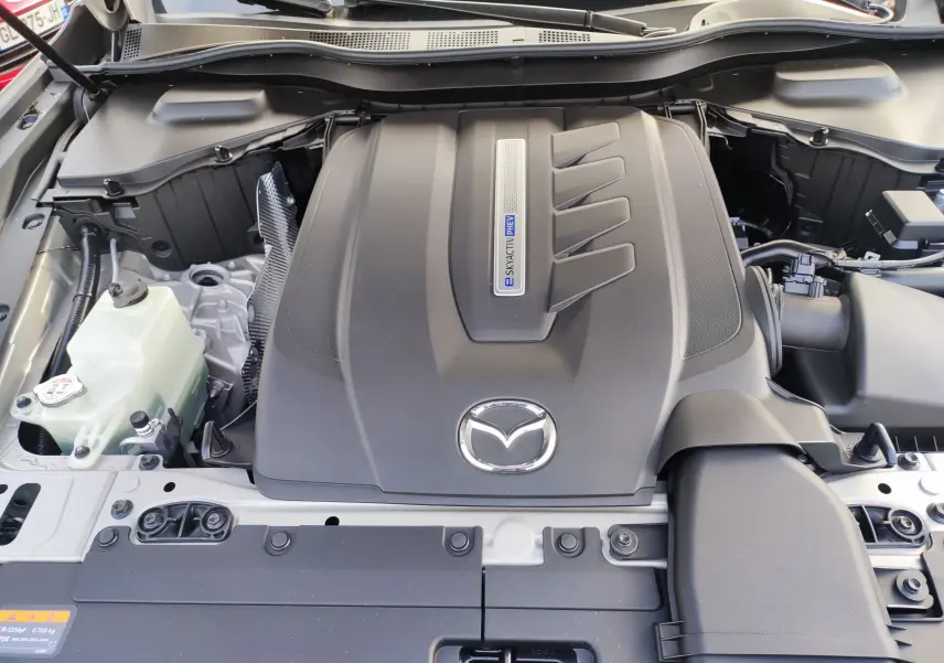 Vue rapprochée du moteur hybride rechargeable du Mazda CX-60 blanc métal avec logo Mazda et inscription Skyactiv PHEV.