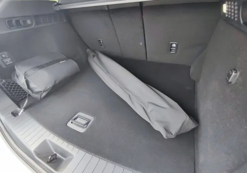 Vue intérieure du coffre noir du Mazda CX-60 2024 avec sac et housse d'accessoires posés au sol.