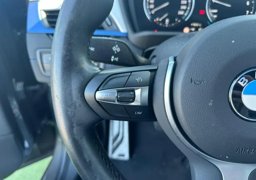 Gros plan sur le volant cuir M de BMW X2 gris foncé, avec commandes multifonctions et tableau de bord flou en arrière-plan.