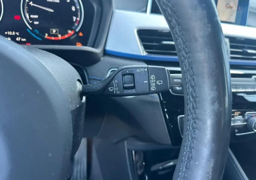 Gros plan sur la commande d’essuie-glace à gauche du volant cuir noir dans l’habitacle gris et bleu d’une BMW X2 2020.