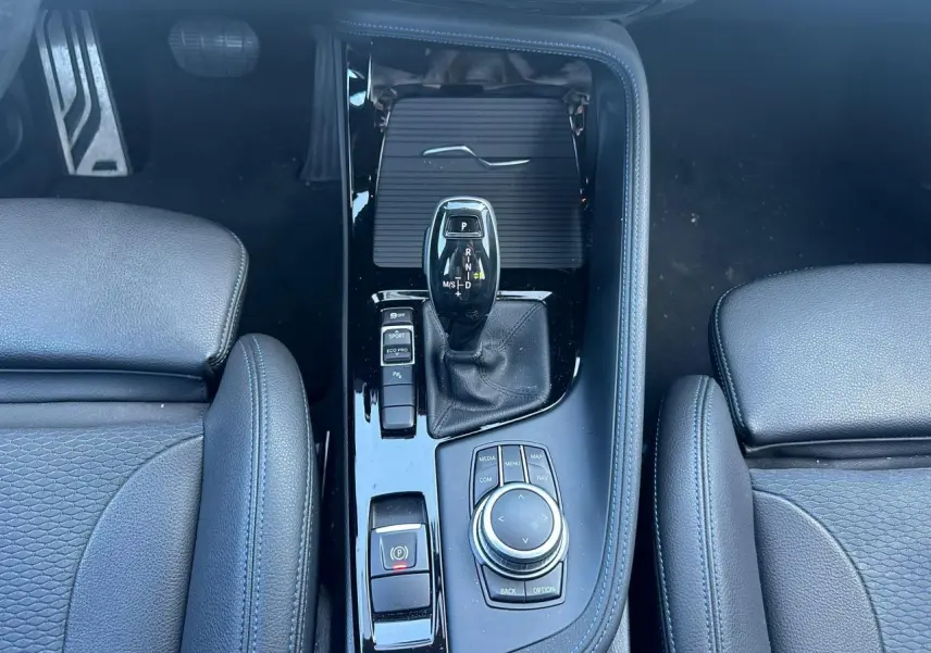 Vue plongeante sur la console centrale noire brillante du BMW X2 avec levier de vitesses automatique et commandes de mode de conduite.