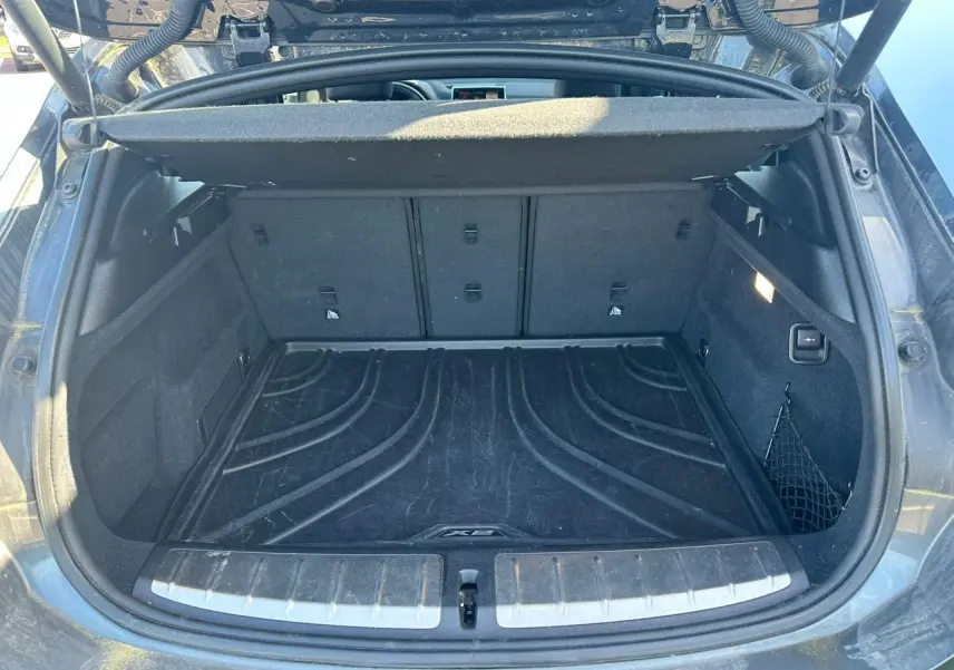 Coffre ouvert vu de l'arrière d'un BMW X2 gris foncé avec tapis de protection et filet latéral.