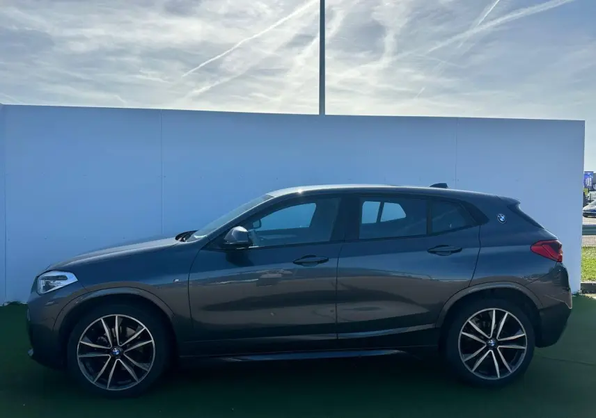 Vue de profil côté gauche d'un BMW X2 gris foncé avec jantes alliage 19 pouces et logo M Sport sur custode.