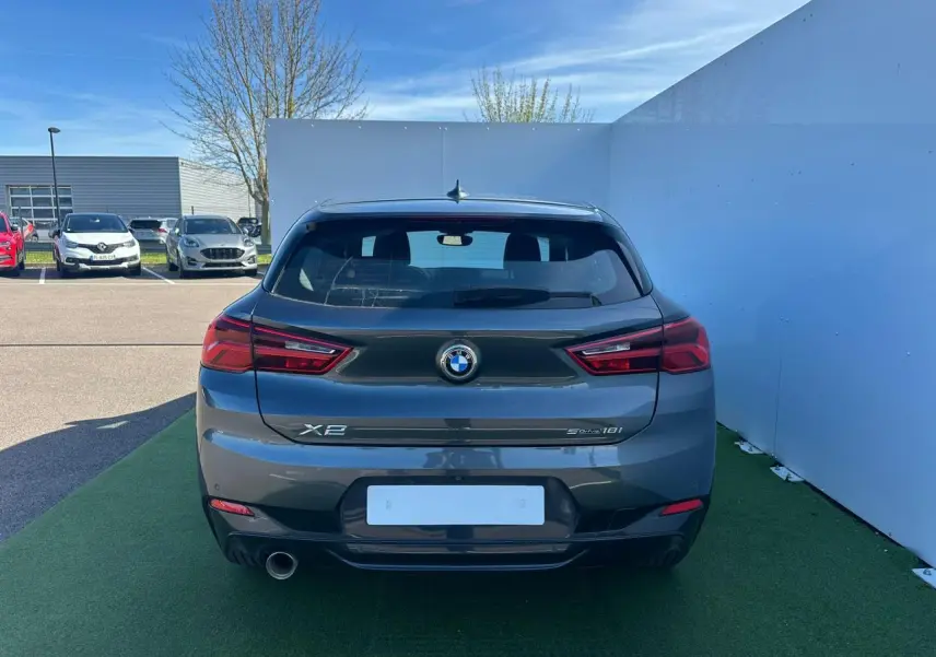 Vue arrière d'une BMW X2 gris foncé avec sortie d'échappement chromée et feux arrière LED, stationnée sur sol vert.