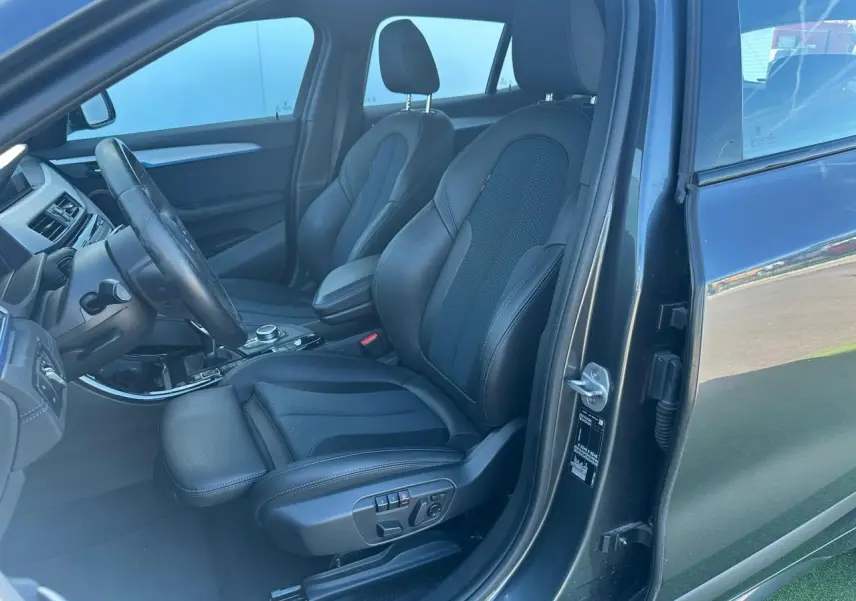 Vue intérieure côté conducteur d'une BMW X2 gris foncé, mettant en valeur les sièges sport en tissu et similicuir avec réglages électriques.