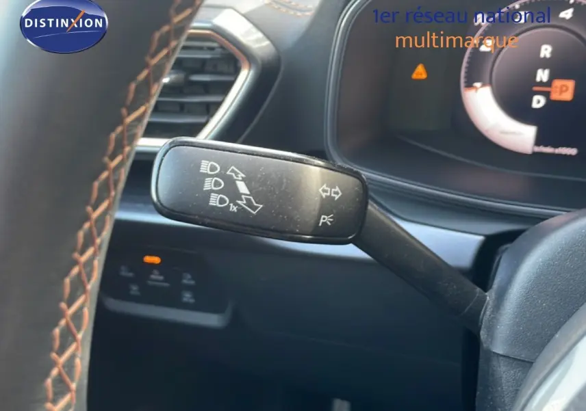 Gros plan sur la commande de clignotants à gauche du volant d’un CUPRA Formentor blanc neige métal, tableau de bord numérique visible.