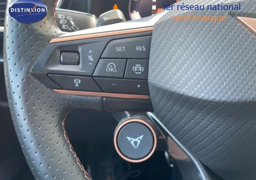 Gros plan sur le volant en cuir perforé avec commandes intégrées et logo CUPRA au centre, intérieur noir.