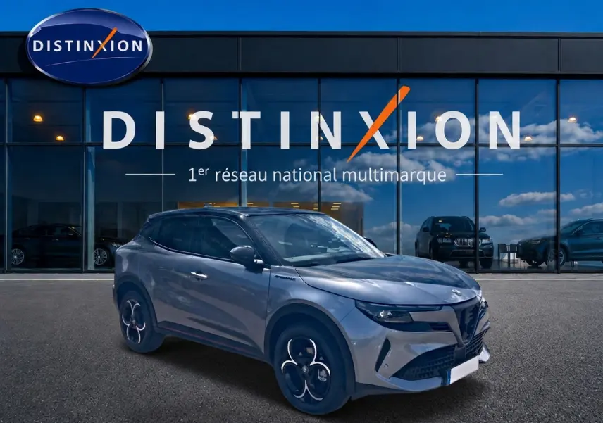 Vue 3/4 avant droit d'une Alfa Romeo Junior 1.2 hybride gris foncé avec jantes alliage et vitres teintées devant un showroom Distinxion.