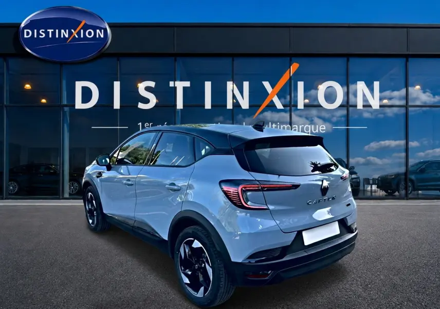 Vue 3/4 arrière droite du Renault Captur gris rafale avec toit noir, jantes alu et feux arrière LED, devant un showroom Distinxion.