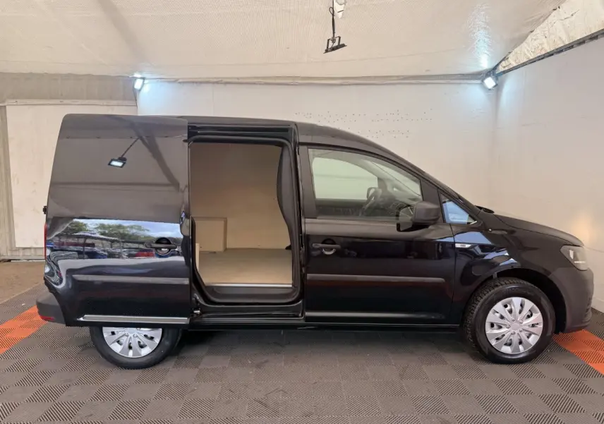 Profil droit d’un Volkswagen Caddy noir 2019 avec porte coulissante ouverte montrant l’espace de chargement vide.