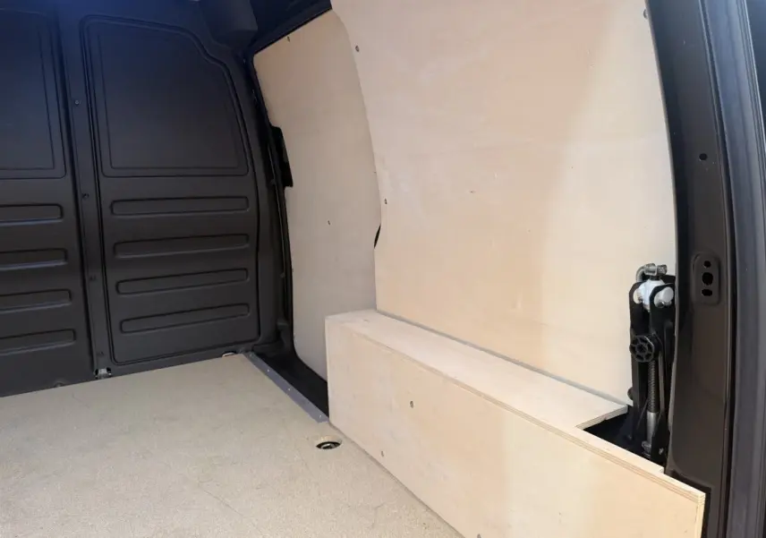 Vue intérieure du coffre arrière du Volkswagen Caddy noir 2019, montrant la cloison pleine en bois clair.