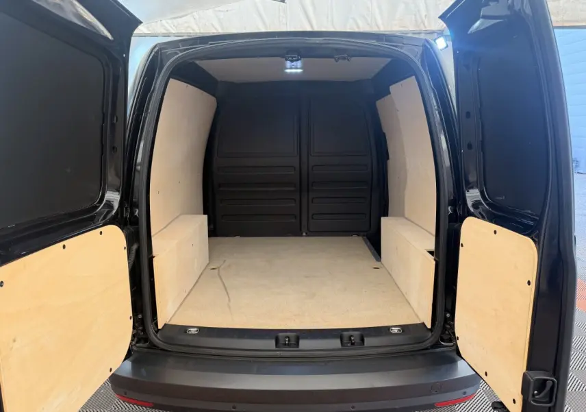 Vue arrière du Volkswagen Caddy noir 2019, montrant l'espace de chargement vide avec habillage bois clair.