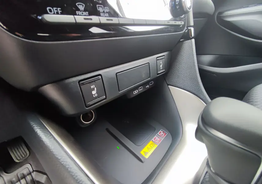 Gros plan sur la console centrale côté passager de la Mazda2 Hybrid 2024, montrant les commandes de sièges chauffants et un chargeur sans fil.