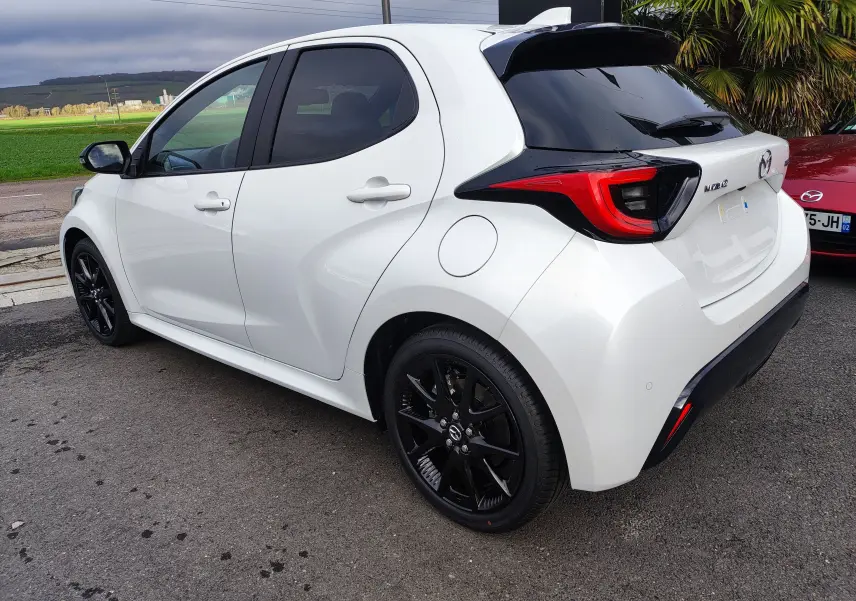 Vue 3/4 arrière droite d'une Mazda2 Hybrid blanche métallisée avec jantes noires et feux arrière distinctifs.