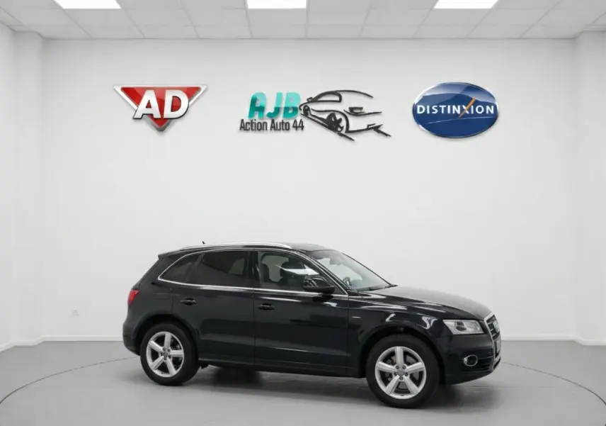 Audi Q5 noir vue de profil côté gauche dans un studio avec logos de concessionnaires en arrière-plan.