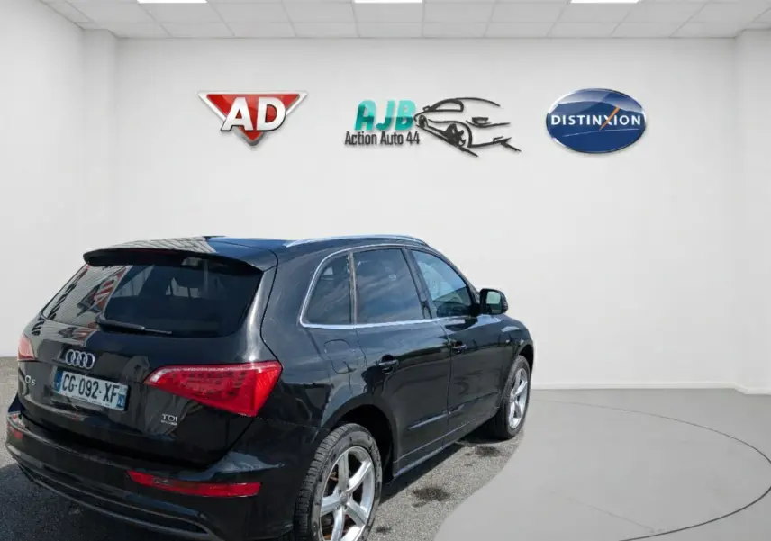 Audi Q5 noir vue 3/4 arrière droit dans un showroom, avec jantes alliage et feux arrière LED distinctifs.