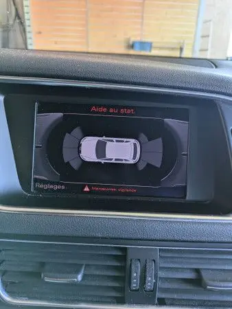 Écran intérieur montrant l'aide au stationnement de l'Audi Q5 noir, vue du tableau de bord côté conducteur.