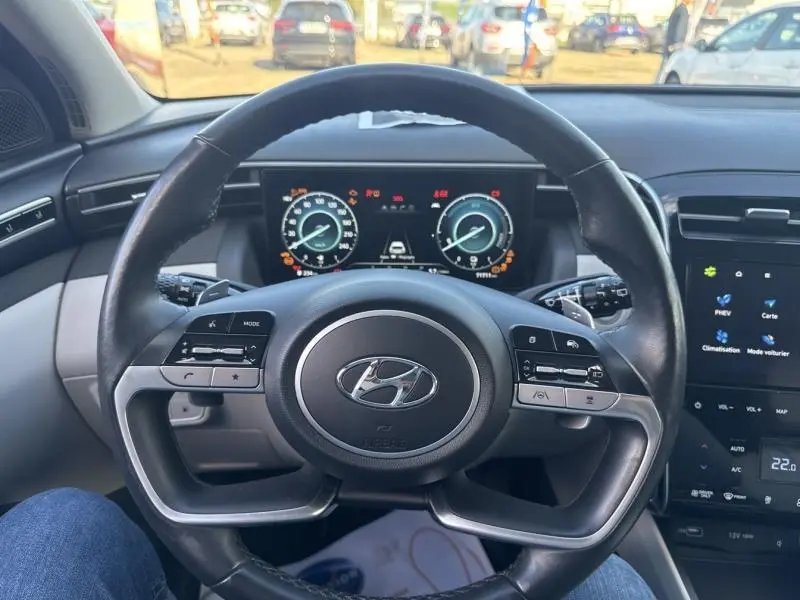 Vue intérieure centrée sur le volant cuir multifonction d'un Hyundai Tucson 2021 avec tableau de bord numérique et écran tactile.