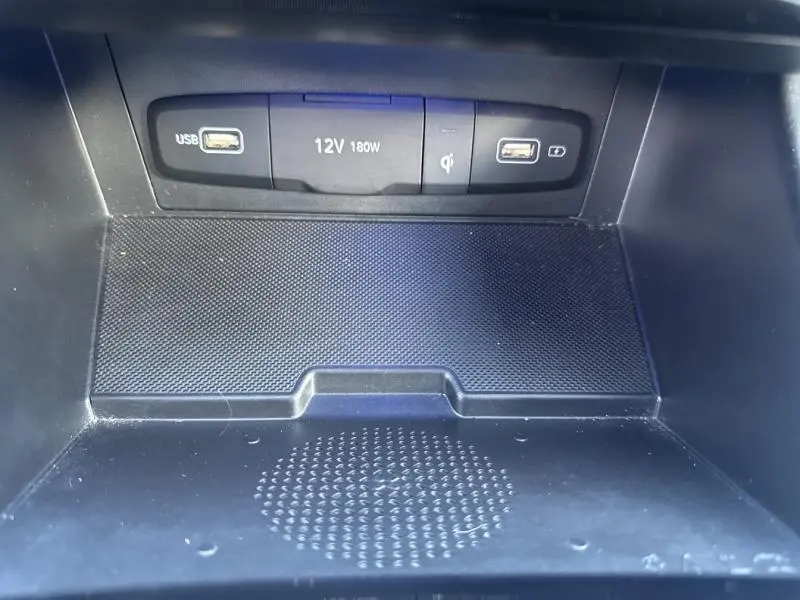 Gros plan sur la console centrale du Hyundai Tucson 2021 montrant ports USB, prise 12V et chargeur sans fil noir.