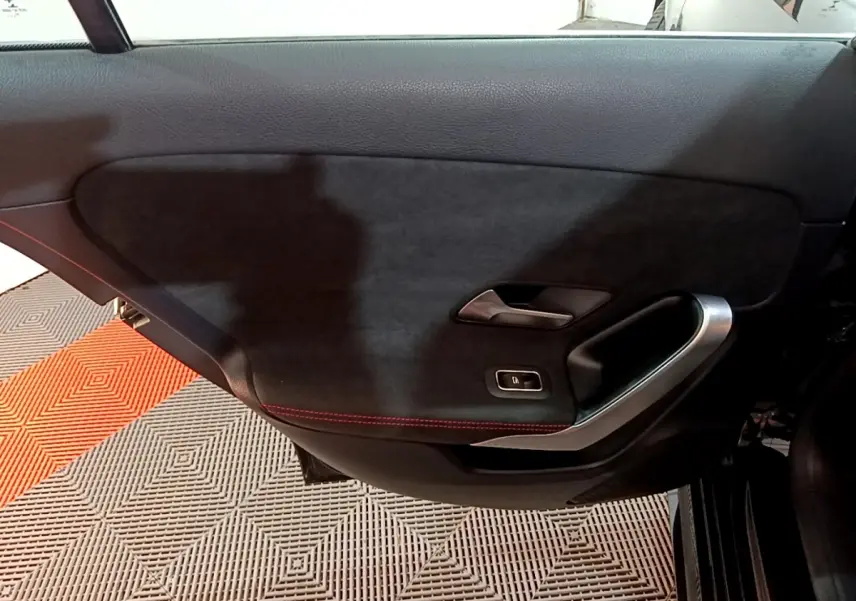Vue intérieure du panneau de porte côté droit noir avec surpiqûres rouges et poignée argentée de la Mercedes Classe A 200 AMG Line.
