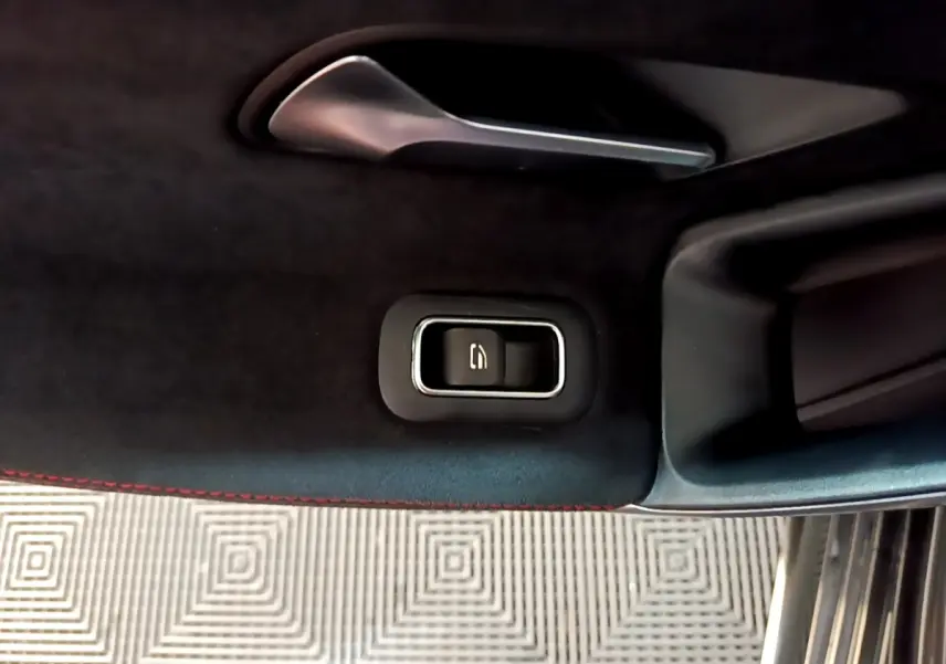 Détail intérieur montrant la commande électrique de la fermeture du coffre sur la porte côté droit, finition noire avec surpiqûres rouges.