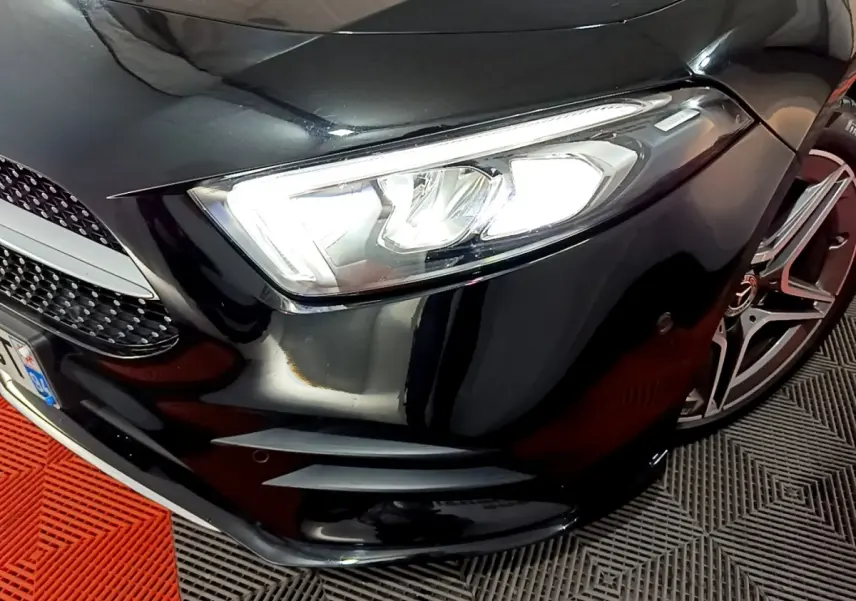 Gros plan sur le phare avant droit et la calandre noire brillante d'une Mercedes Classe A 200 AMG Line 2021.