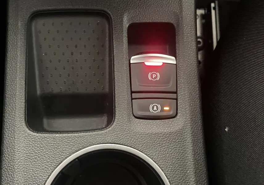 Gros plan sur la console centrale noire du Renault Captur rouge, avec bouton frein à main électronique et arrêt auto allumés.