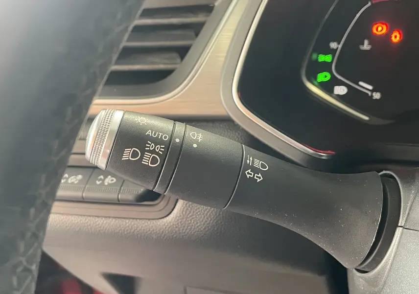 Gros plan sur la commande des feux et clignotants à gauche du volant d’un Renault Captur rouge, tableau de bord partiellement visible.
