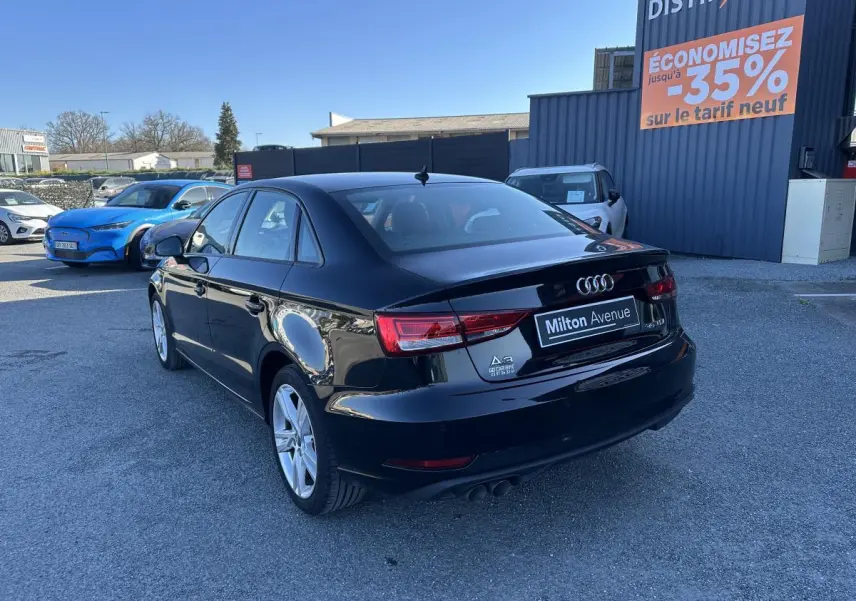 Audi A3 berline noire vue en 3/4 arrière droit, avec jantes aluminium et logo distinctif sur parking extérieur.