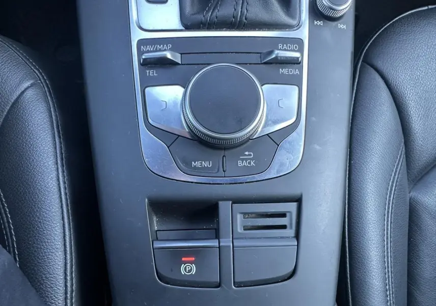 Vue plongeante sur la console centrale noire de l'Audi A3 2020 avec commandes multimédia et frein à main électrique.