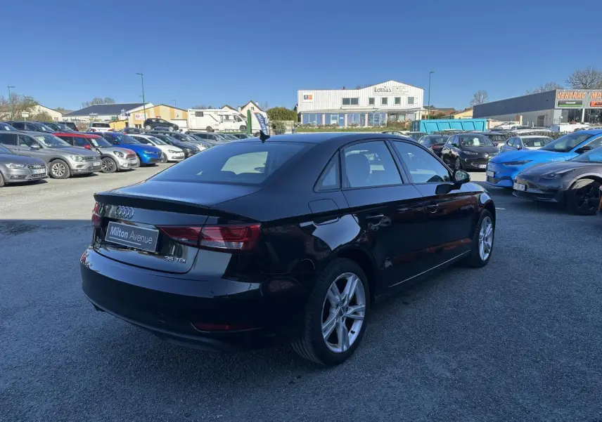 Audi A3 berline noire vue en 3/4 arrière droit sur un parking avec jantes aluminium 10 branches.