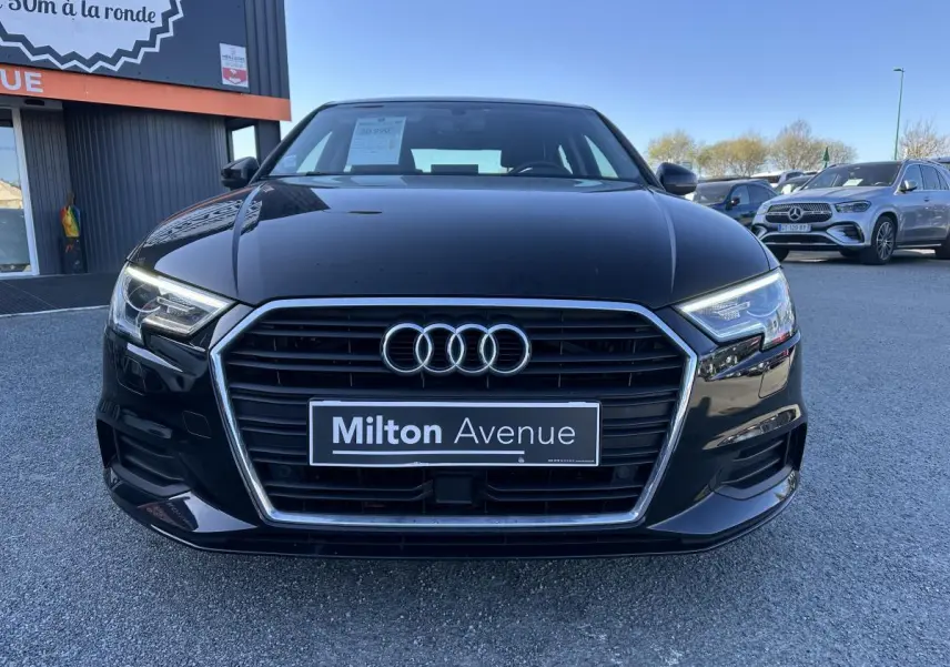 Vue frontale d'une Audi A3 berline noire 2020 avec calandre chromée et phares LED allumés, stationnée en extérieur.