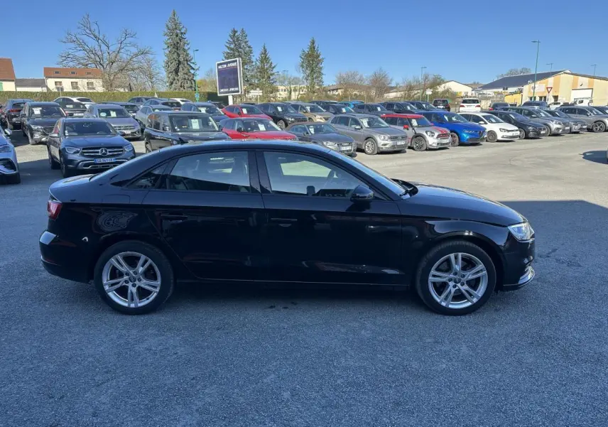 Audi A3 berline noire vue de profil côté gauche sur un parking en extérieur par temps clair.