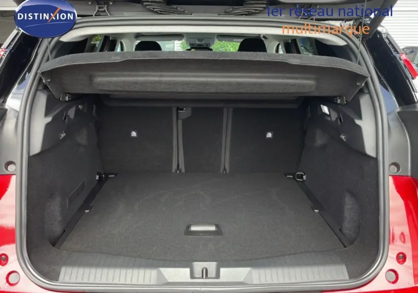 Coffre ouvert vu de l'arrière d'un Citroën C5 Aircross Hybrid rouge rubis métal, espace de chargement spacieux et tapis noir.