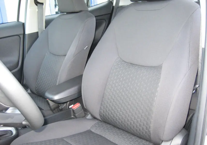 Gros plan sur les sièges avant noirs de la Toyota Yaris Cross 2025, mettant en valeur leur tissu texturé et l'accoudoir central.