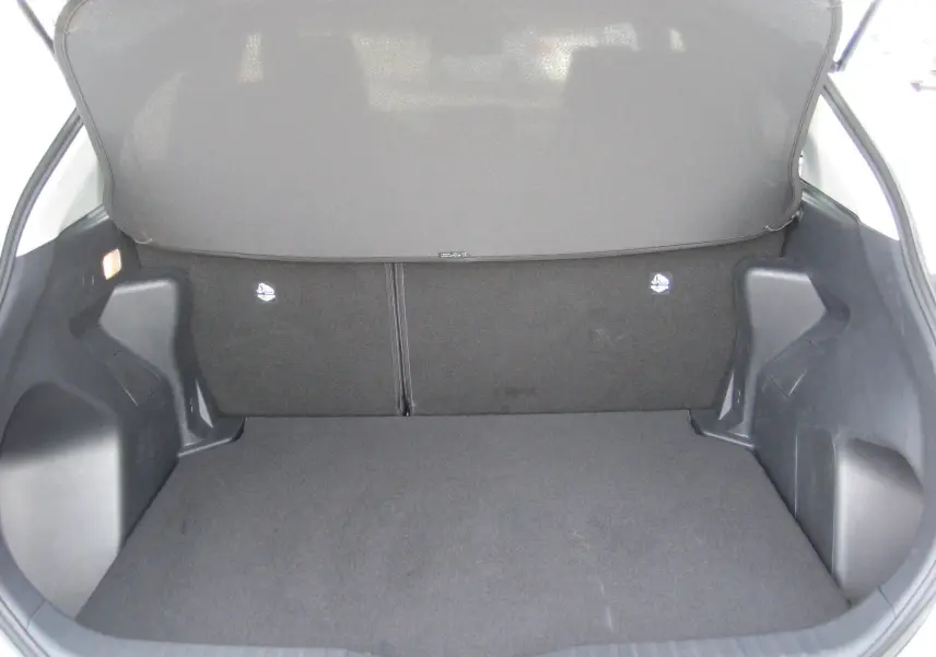 Coffre ouvert vu de l'arrière d'une Toyota Yaris Cross blanche 2025, espace de chargement vide et tapis noir.