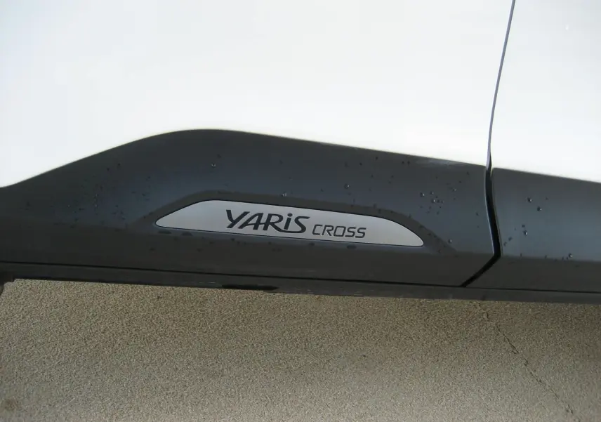Gros plan sur la bas de caisse noir avec logo YARIS CROSS sur une Toyota Yaris Cross blanche.