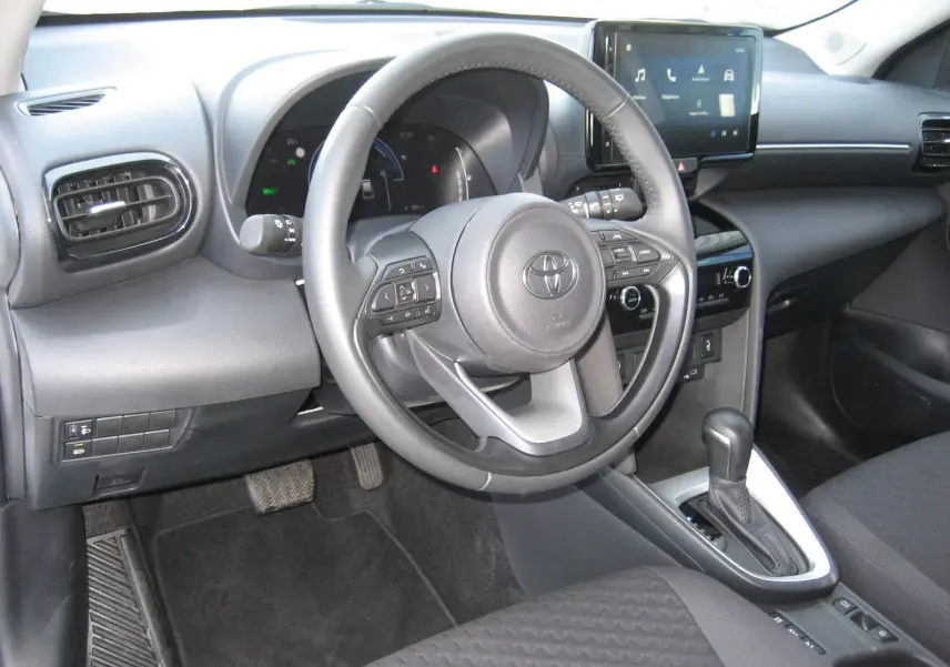 Vue intérieure de la Toyota Yaris Cross 2025, tableau de bord et volant multifonction en noir, avec écran tactile central.