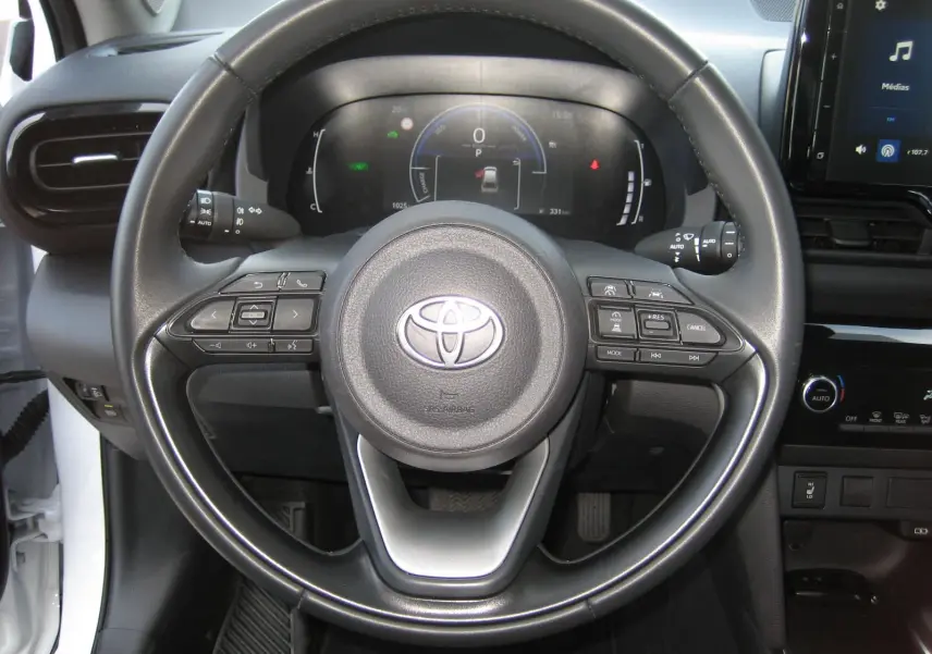 Vue centrée sur le volant noir de la Toyota Yaris Cross blanche 2025, avec tableau de bord digital et commandes intégrées.