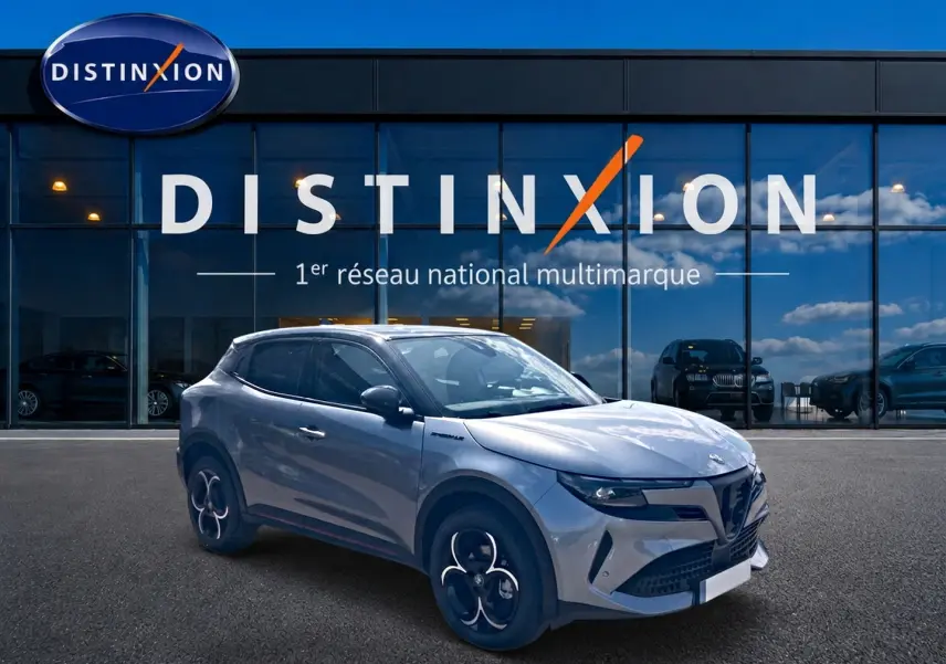 Vue 3/4 avant droit d'une Alfa Romeo Junior 1.2 hybride gris t/noir avec jantes en alliage devant un showroom Distinxion.