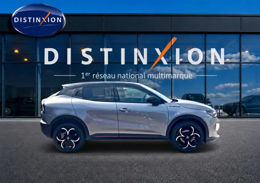 Profil droit d'une Alfa Romeo Junior 1.2 hybride gris foncé avec jantes alliage noires devant une vitrine Distinxion.